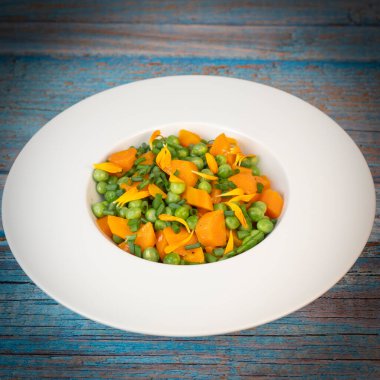 Taze bezelye ve havuçlar tuzlu tereyağıyla pişirilir, sonra frenk soğanı ve parlak kadife çiçekleriyle süslenir..