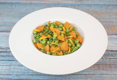 Taze bezelye ve havuçlar tuzlu tereyağıyla pişirilir, sonra frenk soğanı ve parlak kadife çiçekleriyle süslenir..