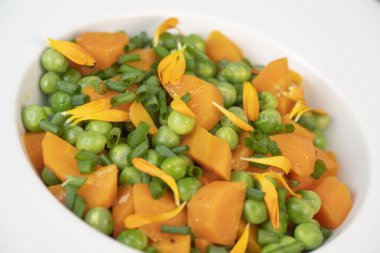 Taze bezelye ve havuçlar tuzlu tereyağıyla pişirilir, sonra frenk soğanı ve parlak kadife çiçekleriyle süslenir..