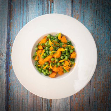 Taze bezelye ve havuçlar tuzlu tereyağıyla pişirilir, sonra frenk soğanı ve parlak kadife çiçekleriyle süslenir..