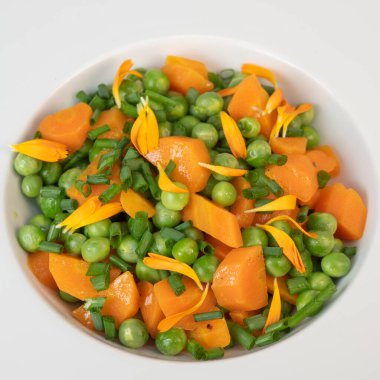 Taze bezelye ve havuçlar tuzlu tereyağıyla pişirilir, sonra frenk soğanı ve parlak kadife çiçekleriyle süslenir..