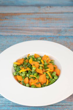 Taze bezelye ve havuçlar tuzlu tereyağıyla pişirilir, sonra frenk soğanı ve parlak kadife çiçekleriyle süslenir..