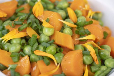 Taze bezelye ve havuçlar tuzlu tereyağıyla pişirilir, sonra frenk soğanı ve parlak kadife çiçekleriyle süslenir..