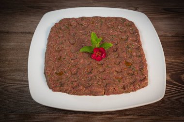 Kebbe naye, zengin bir mutfak deneyimi için tasarlanmış bulgur, soğan, nane ve baharatla karıştırılmış ince doğranmış çiğ et içeren beyaz bir tabakta sergileniyor..