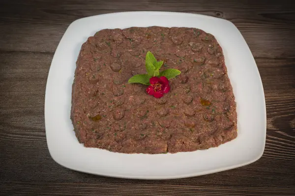 Kebbe naye, zengin bir mutfak deneyimi için tasarlanmış bulgur, soğan, nane ve baharatla karıştırılmış ince doğranmış çiğ et içeren beyaz bir tabakta sergileniyor..