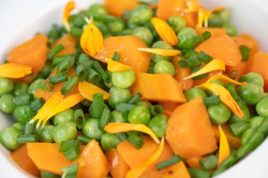 Taze bezelye ve havuçlar tuzlu tereyağıyla pişirilir, sonra frenk soğanı ve parlak kadife çiçekleriyle süslenir..