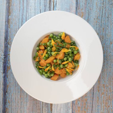 Taze bezelye ve havuçlar tuzlu tereyağıyla pişirilir, sonra frenk soğanı ve parlak kadife çiçekleriyle süslenir..