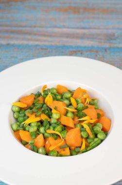 Taze bezelye ve havuçlar tuzlu tereyağıyla pişirilir, sonra frenk soğanı ve parlak kadife çiçekleriyle süslenir..