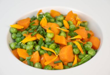 Taze bezelye ve havuçlar tuzlu tereyağıyla pişirilir, sonra frenk soğanı ve parlak kadife çiçekleriyle süslenir..