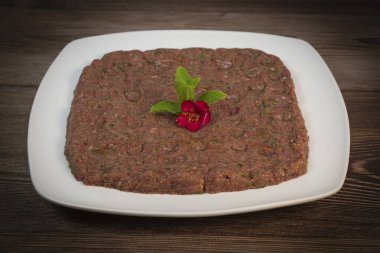 Kebbe naye, zengin bir mutfak deneyimi için tasarlanmış bulgur, soğan, nane ve baharatla karıştırılmış ince doğranmış çiğ et içeren beyaz bir tabakta sergileniyor..