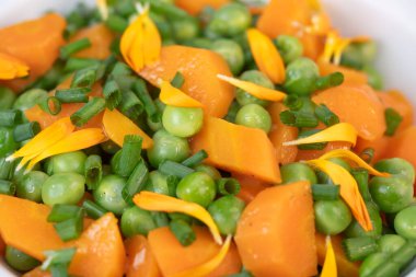 Taze bezelye ve havuçlar tuzlu tereyağıyla pişirilir, sonra frenk soğanı ve parlak kadife çiçekleriyle süslenir..