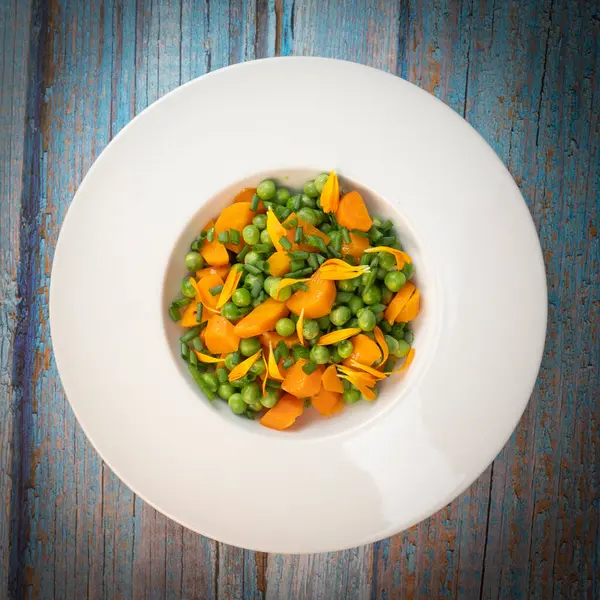 Taze bezelye ve havuçlar tuzlu tereyağıyla pişirilir, sonra frenk soğanı ve parlak kadife çiçekleriyle süslenir..