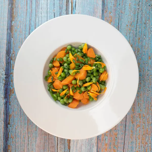 Taze bezelye ve havuçlar tuzlu tereyağıyla pişirilir, sonra frenk soğanı ve parlak kadife çiçekleriyle süslenir..