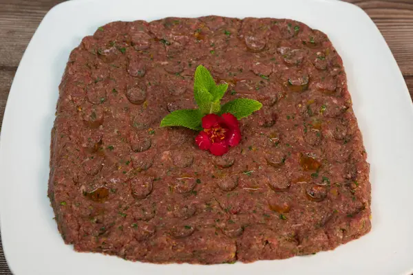 Kebbe naye, zengin bir mutfak deneyimi için tasarlanmış bulgur, soğan, nane ve baharatla karıştırılmış ince doğranmış çiğ et içeren beyaz bir tabakta sergileniyor..