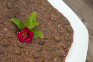 Kebbe naye, zengin bir mutfak deneyimi için tasarlanmış bulgur, soğan, nane ve baharatla karıştırılmış ince doğranmış çiğ et içeren beyaz bir tabakta sergileniyor..