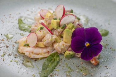 Avokado ve turpla tamamlanmış taze dorade ve karideslerle yapılmış lezzetli ceviche, huzur verici yeşil bir tabakta yenilebilir bir çiçekle süslenmiş..