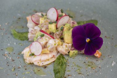 Avokado ve turpla tamamlanmış taze dorade ve karideslerle yapılmış lezzetli ceviche, huzur verici yeşil bir tabakta yenilebilir bir çiçekle süslenmiş..