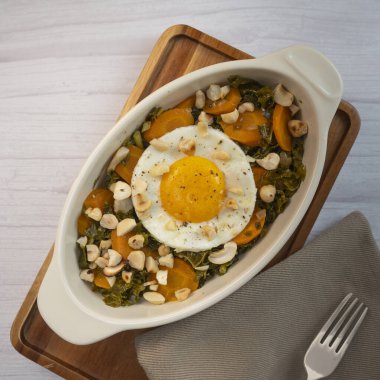 Recipe for kale, carrot and garlic poellee, chopped hazelnuts, cashews and almonds, and fried egg with toasted garlic bread and olive oil