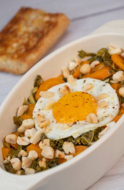 Recipe for kale, carrot and garlic poellee, chopped hazelnuts, cashews and almonds, and fried egg with toasted garlic bread and olive oil
