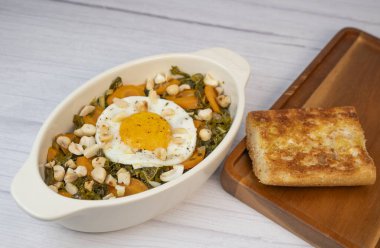 Recipe for kale, carrot and garlic poellee, chopped hazelnuts, cashews and almonds, and fried egg with toasted garlic bread and olive oil