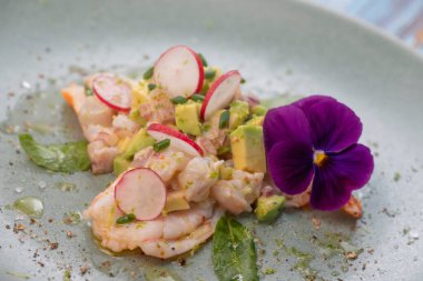 Avokado ve turpla tamamlanmış taze dorade ve karideslerle yapılmış lezzetli ceviche, huzur verici yeşil bir tabakta yenilebilir bir çiçekle süslenmiş..