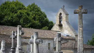 Süslü taş haçlarla dolu bir mezarlık Saint-Laurent-des-Combes 'daki tarihi bir kilisenin yanında duruyor..