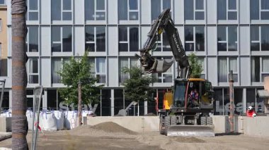 Fransa, Toulouse, Ağustos 2025, büyük kazıcı işlek bir kentsel alandaki inşaat sahasında toprak kazıyor ve taşıyor. Yakınlarda, yüksek binalar ve yeşillik devam eden iş için zemin hazırlıyor.