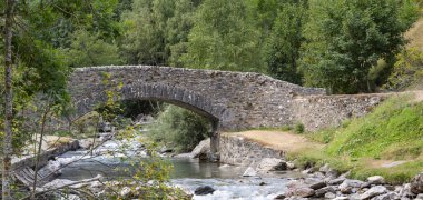 Pireneler 'deki akan Gavarnie deresini çevreleyen taştan bir köprü, canlı ağaçlar ve yüksek dağlarla çevrili, sabahın erken saatlerinde huzurlu ve pitoresk bir atmosfer yaratıyor..
