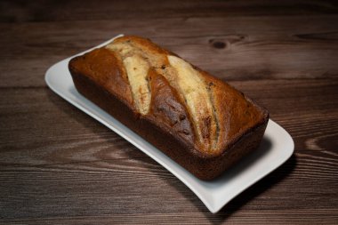 A freshly baked banana bread gateau is displayed on a white plate, showcasing its golden-brown crust and ripe banana slices on top. Perfect for a sweet treat or dessert.