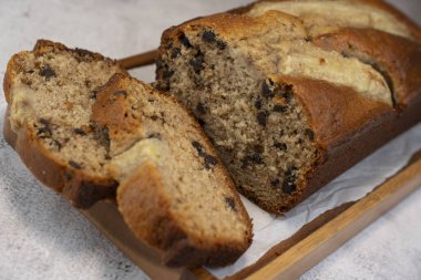 Freshly baked banana bread is sliced and displayed on a wooden cutting board. The bread has a golden-brown crust and chocolate chips, perfect for a cozy snack at home.