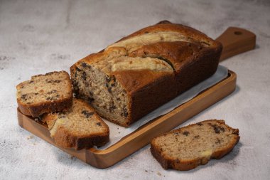 Freshly baked banana bread is sliced and displayed on a wooden cutting board. The bread has a golden-brown crust and chocolate chips, perfect for a cozy snack at home.