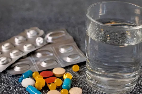 Temiz bir yüzeyde bir bardak suyun yanına yerleştirilmiş haplar. İlaç, sağlık, günlük takviye ve tıbbi tedavi kavramı. İlaç reklamcılığı, sağlık eğitimi ve refah içeriği için mükemmel.