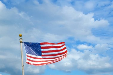 Amerikan bayrağı bulutlu parlak bir gökyüzüne doğru dalgalanıyor. Özgürlüğün, vatanseverliğin ve ABD 'nin ulusal gururunun sembolü.