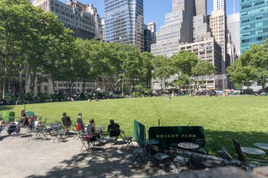 New York, Stati Uniti - 19 Maggio 2025 Kentsel yaşam tarzı sahnesi Bryant Park, New York 'ta, insanların yeşil ve uzun gökdelenlerle çevrili banklarda ve sandalyelerde oturup rahatladıkları