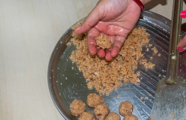 stock image High angle view of a woman making homemade sweet, coconut laddu for festive season on a domestic table. Close up and selective focus.