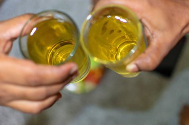 Gri bir masada gri bir arka planda iki Hintli adamın elleri viski bardaklarını tokuşturuyor. Sıvıya seçici odaklanma.