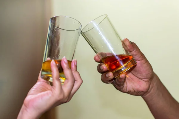 An Indian couple\'s hands makes a toast with two glasses of whiskey. Selective focus on man\'s hand.