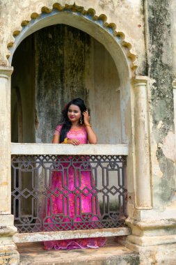 Serene woman standing by a mandir and contemplating while looking away at something with a blank expression.