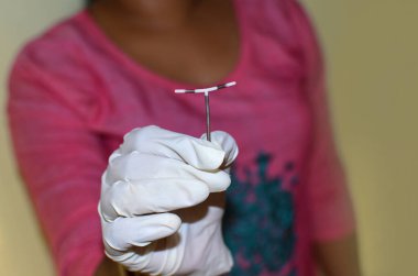 Rahminden çıkarıldıktan sonra beyaz zemin üzerinde T şeklinde doğum kontrol cihazı tutan doktor, yakın plan ve seçici olarak doğum kontrol cihazına odaklanıyor..
