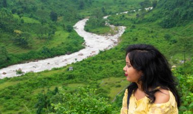 Genç Hintli kadın arka planda vahşi orman, dağlar ve nehirle tek başına oturuyor. Seyahat tarzı ve hayatta kalma kavramı..