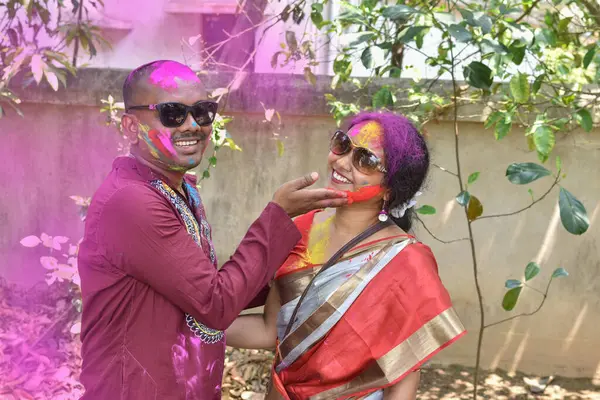 stock image Indian man putting colour on a woman's face during holi celebration at outdoor park.