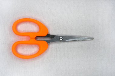 Beyaz arka planda kıvrımlı ve sivri uçlu küçük bir makas. Paslanmaz çelik bıçaklı turuncu kupür defteri makası. El sanatları için küçük eğimli iplik makası.