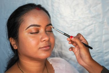 Evde çalışan tanınmayan bir makyaj sanatçısının göz kapaklarını kadın bir müşterinin göz kapaklarına sürterek görüntüsü..