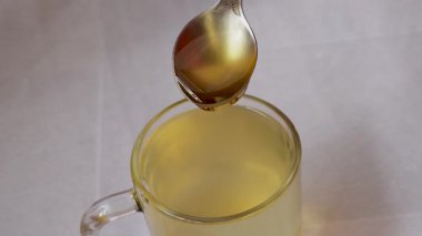 Birisi gümüş bir kaşık tutuyor ve beyaz arka planda zencefil, limon ve zerdeçal ile yapılmış bitki çayıyla dolu bir bardağa bal döküyor. Kopyalama alanı ile seçmeli odak.