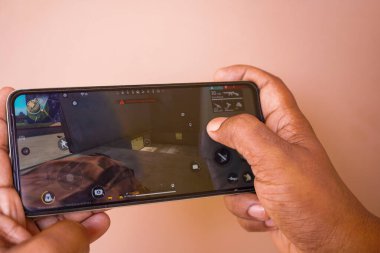 Batı Bengal, Hindistan - 16 Mayıs 2025: Genç bir adam akıllı telefonda PUBG oyunu oynuyor. Genç bir çocuk elinde bir oyunla bir telefon tutuyor Bilinmeyen Oyuncuların Savaş Alanında gri bir arka planda.