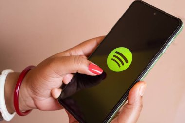 West Bengal, Hindistan - 16 Mayıs 2025: Bir kadın bir kafedeki masada otururken iPhone 'unda Spotify uygulamasını kullanıyor. Spotify logosu akıllı telefon ekranında görüntülenir.