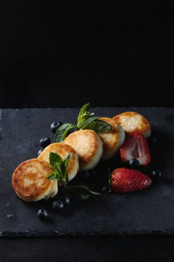 Süzme peynirli krep, siyah arka planda şurup. Yukarıdan beyaz un dökülüyor..