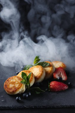 Süzme peynirli krep, siyah arka planda şurup. Yukarıdan beyaz un dökülüyor..