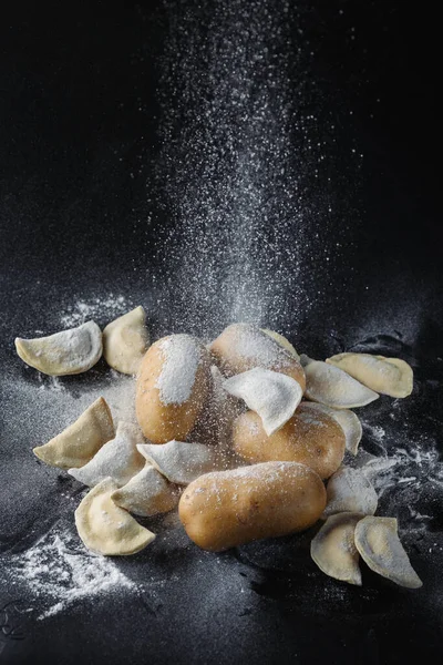 stock image Dumplings, mushrooms and potatoes on a black background are covered with flour