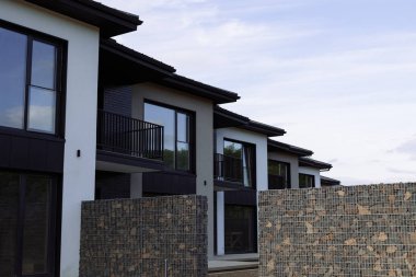 Park ve mavi gökyüzünün arka planında panoramik pencereleri olan birçok modern beyaz kulübe.